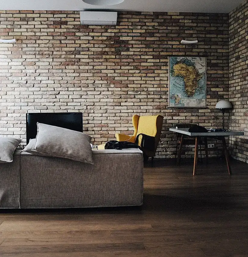 Salón con pared de ladrillo visto, sofá y escritorio, en una vivienda como las que vaciamos en Santa Coloma de Gramenet